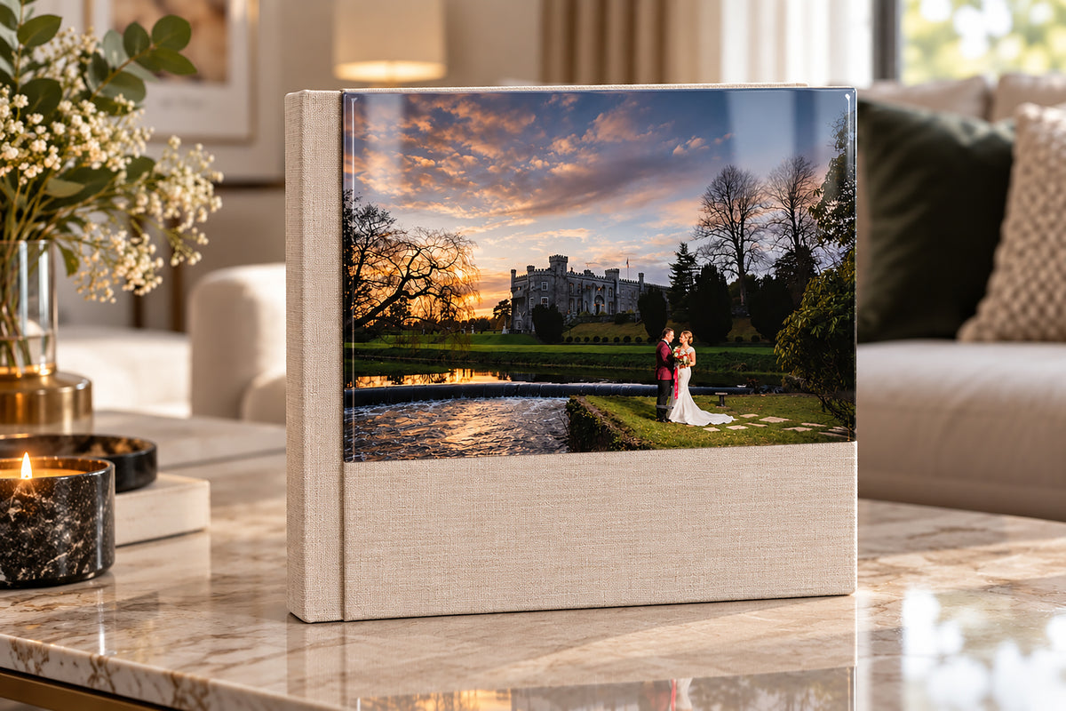 Cappuccino linen wedding album with a half acrylic photo cover showing a castle sunset wedding photo, on a marble coffee table